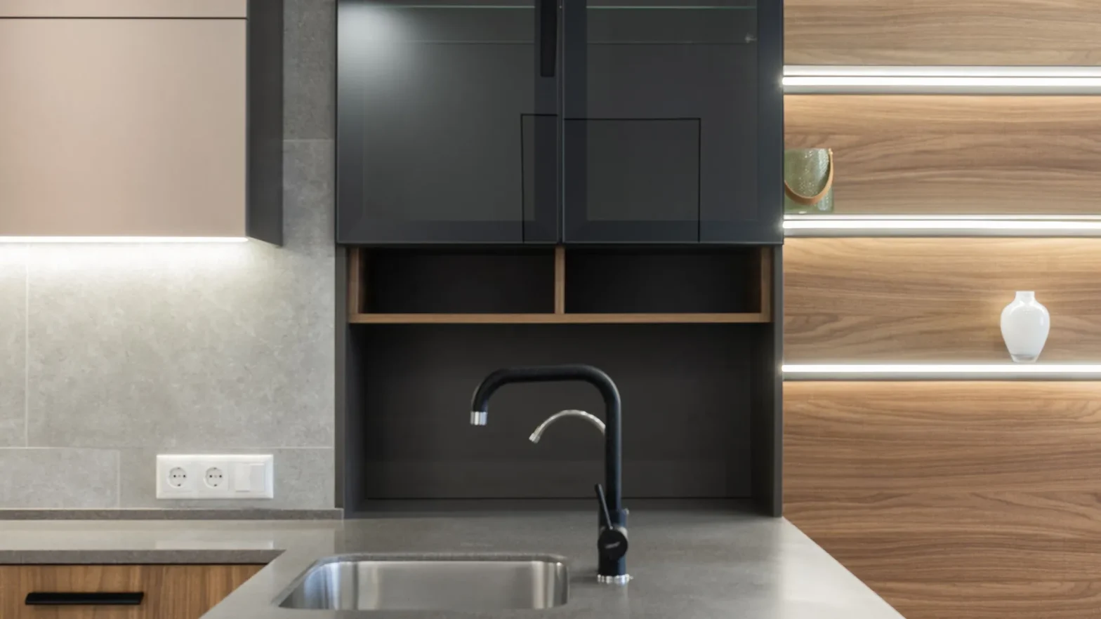 Modern kitchen with dark gray cabinets, wooden open shelves, and a black curved faucet over a gray countertop.