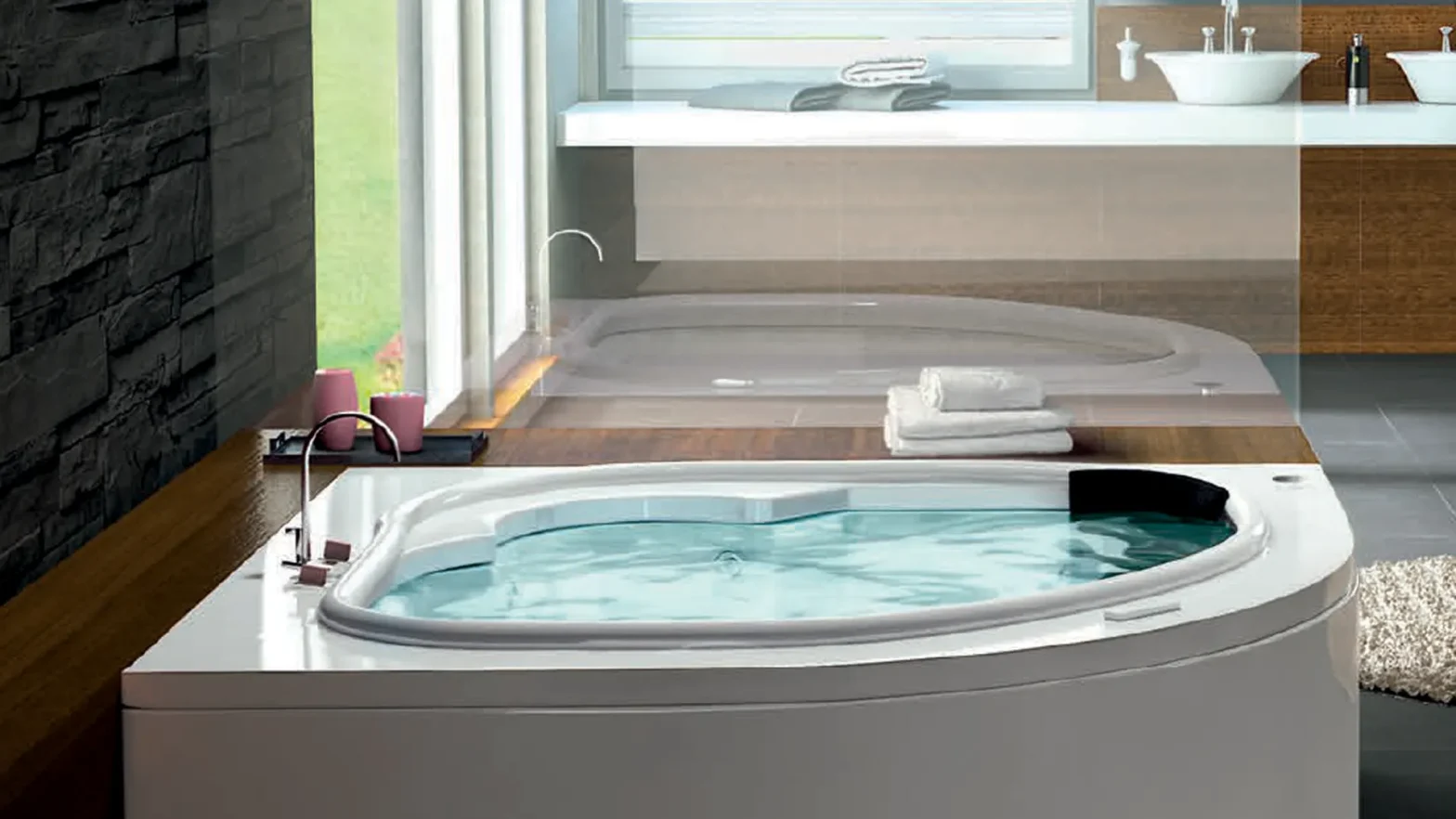 Modern bathroom featuring a built-in whirlpool tub on a wooden deck, stone wall on the left, and a double vanity with towels nearby.