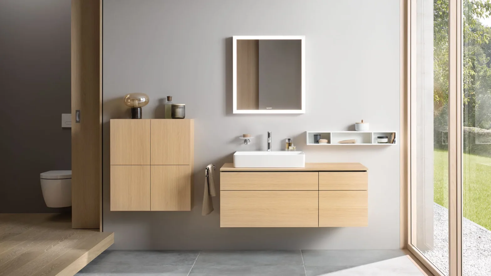 Modern bathroom with a wall-mounted wooden vanity, white rectangular sink, backlit square mirror, and a large glass door showing greenery outside.