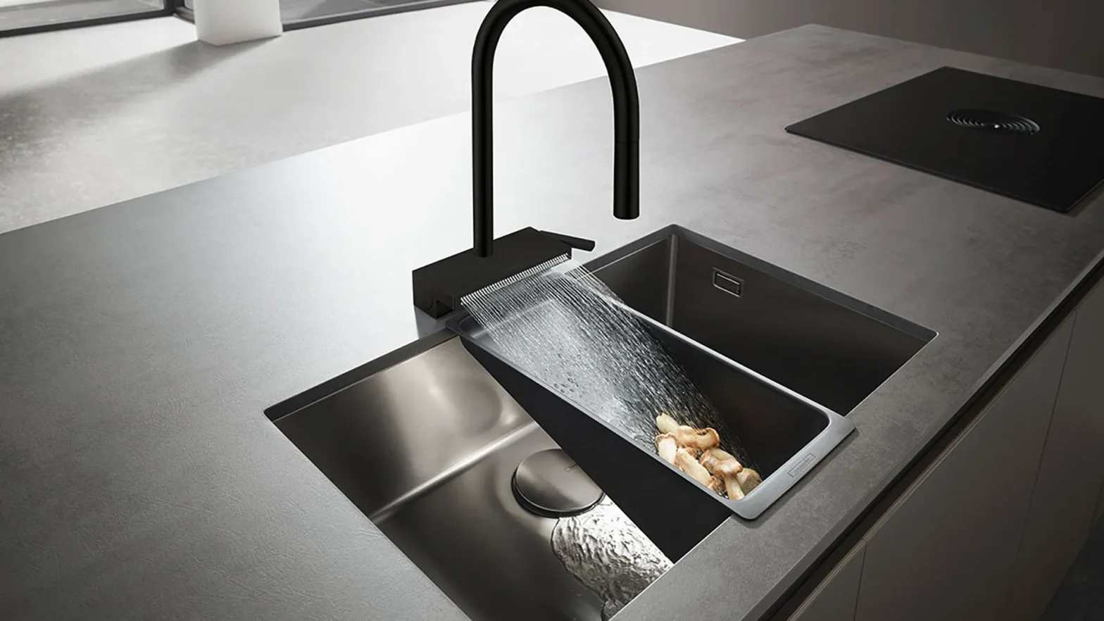 Modern black curved faucet over a stainless steel sink; water streams into a pull-out tray holding potatoes or food pieces.