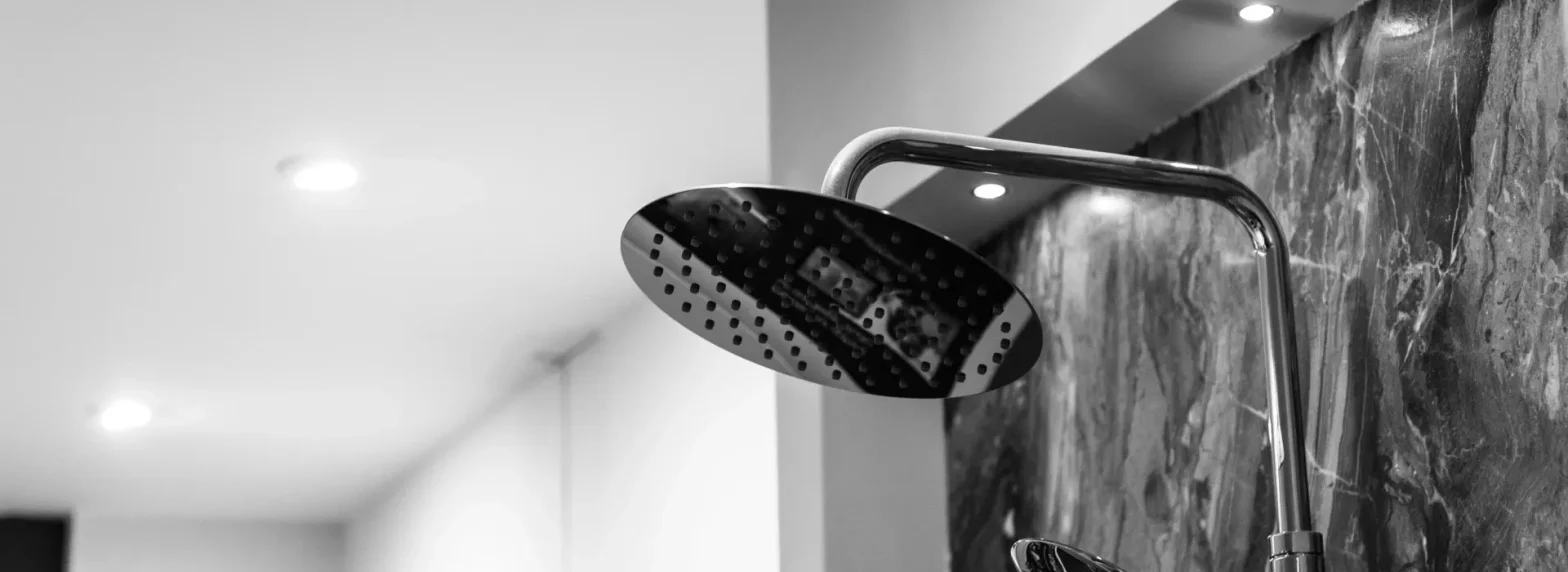 Close-up of a chrome shower head attached to a curved arm against a marble bathroom wall.